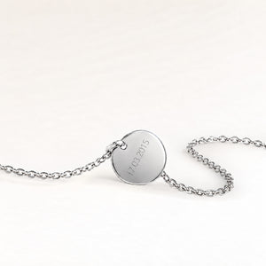 Baksidan av ett runt silverhalsband med personlig gravyr av ett datum