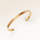 Närbild av minimalistiskt bangle armband i guld med vågig yta och plats för personlig gravyr