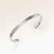 Närbild av minimalistiskt bangle armband i silver med vågig yta och plats för personlig gravyr