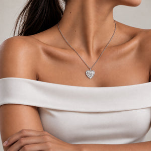 Modell i elfenbensvit off shoulder-topp med hjärtformat silverhalsband med vågig yta och plats för personlig gravyr av text, koordinater eller handstil på baksidan