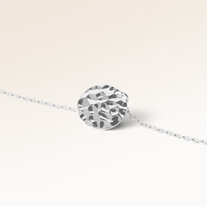 Närbild av minimalistiskt runt berlock i silver med vågig yta och plats för gravyr baktill