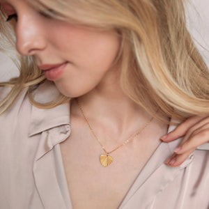 Modell med personligt hjärtformat halsband för kvinnor i guld med räfflat solstrålemönster och gravyr baktill, från Mon Chou.