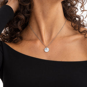 Modell i svart topp med runt silverhalsband med räfflat solstrålemönster och plats för personlig gravyr av text, koordinater eller handstil på baksidan